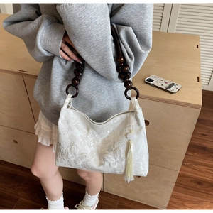 Détail du sac brodé papillon blanc avec bandoulière en perles de bois et pompon