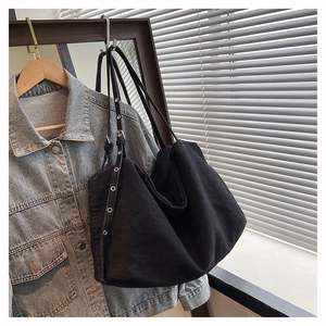 Detail of black canvas tote bag showing wide shoulder strap with silver metal eyelets