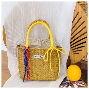 Close-up of straw woven bucket bag with yellow rope handle and On Our Own label