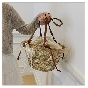 Detail of straw tote bag showing daisy embroidery, lace bow, and leather straps