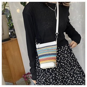 Detail of colorful woven straw crossbody bag with white leather base and shoulder strap