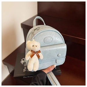 Detail of light blue patent mini backpack with plush bear charm on wooden steps