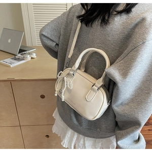 Detail of cream white leather pillow bag with pearl bow charm and shoulder strap