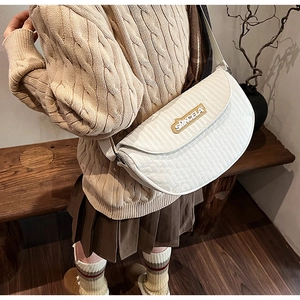 Detail of white quilted saddle bag with yellow logo and wide fabric shoulder strap