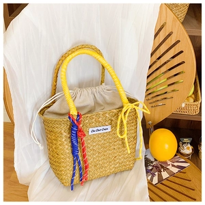 Detail of hand-woven straw bucket bag with colorful knot handle and drawstring canvas liner