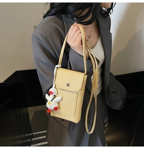 Detail of light yellow crossbody phone bag with litchi texture and cute duck charm