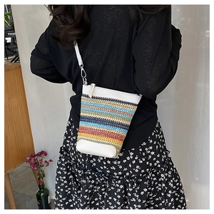 Side view of a colorful striped straw woven crossbody bag with white leather trim details