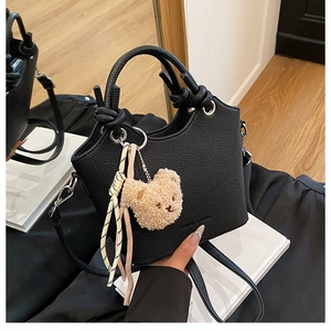 Detailed view of black pebbled leather bucket bag with cute bear charm and woven rope