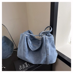 Detail of washed blue denim tote bag with metallic rivet accents and zipper closure