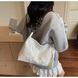 Détail du sac blanc avec broderie papillon, bandoulière en perles de bois et pompons