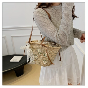Detail of straw bucket bag featuring white daisy embroidery and lace bow decoration