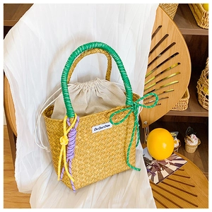 Close-up of woven straw bucket bag with green rope handle and colorful decorative knots