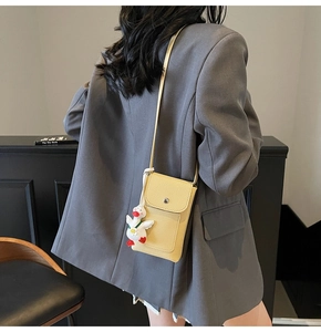 Detail of yellow lychee texture phone bag with cute duck charm on grey blazer