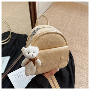 Detail of cream mini backpack featuring crinkled patent texture and teddy bear pendant