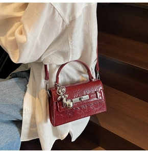 Detail of dark red pleated leather crossbody bag with silver lock and dog charm on stairs