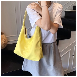 Detail of minimalist bright yellow nylon tote bag worn by a model against a modern staircase