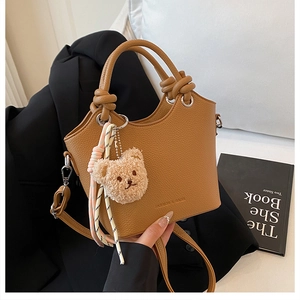Close-up of brown litchi pattern bucket bag featuring a knot handle and bear charm