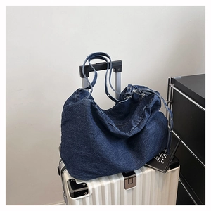 Detail of dark blue denim tote bag placed on a white suitcase for travel styling