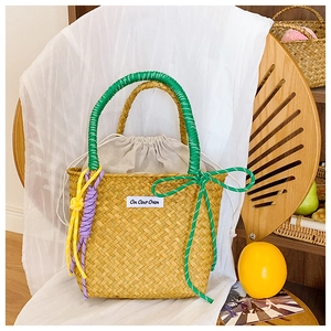 Detail of straw woven bucket bag with green handles and colorful decorative charms