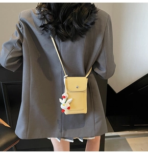 Detail view of yellow litchi leather phone bag with a cute white duck plush keychain