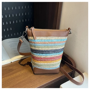 Detail of colorful woven straw crossbody bag featuring brown leather trim and metal zipper