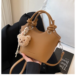 Detail of camel bucket bag with leather texture, knotted handle, and cute bear charm