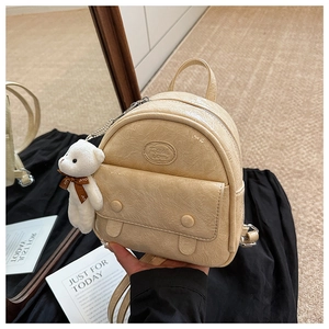 Detail of vintage beige mini backpack with faux leather texture and a plush bear charm