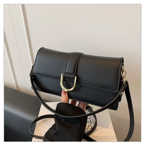 Détail du sac sous le bras en cuir noir avec boucle en métal doré et rabat sur le dessus