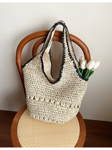 Large woven straw shoulder bag with contrast black trim and hollow patterns on a wooden chair