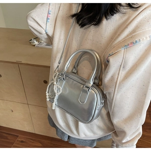 Detail of silver metallic Boston bag featuring decorative pearl and heart charms