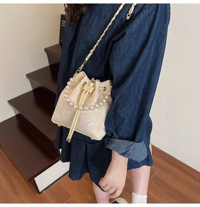 Détail du sac seau en soie beige avec broderie papillon dorée et poignée en perles
