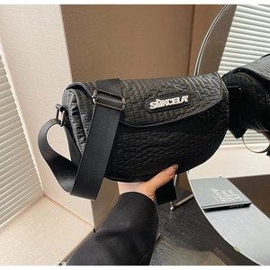 Detail of black quilted shoulder bag featuring adjustable wide strap and logo tag