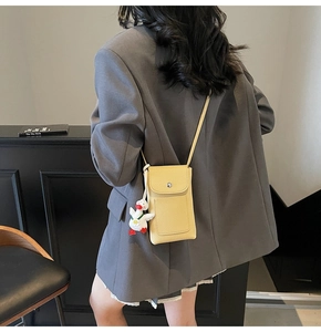 Detail of yellow pebbled leather mini crossbody bag with a cute white duck plush charm