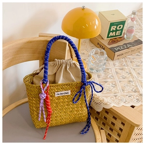 Detail of straw woven bucket bag featuring blue spiral handles and brand label on a wooden chair