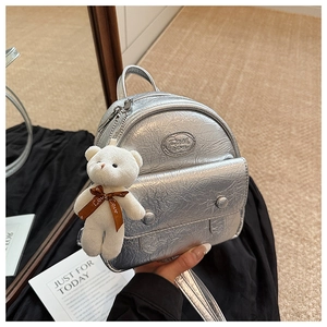 Detail of silver metallic mini backpack with crinkled texture and plush bear accessory