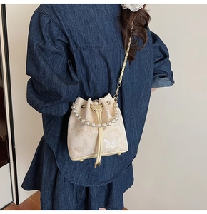 Détail du sac seau crème à cordon avec broderie dorée et poignée en perles