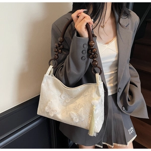 Détail du sac cabas blanc avec broderie papillon, poignée en bois et pompon décoratif