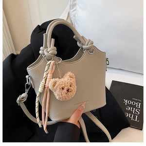 Detail of grey pebbled bucket bag featuring knotted handle and plush bear charm accent