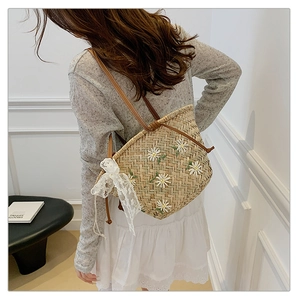 Detail of straw bucket bag featuring white daisy embroidery and a lace bow charm
