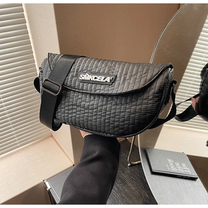 Detailed view of the black quilted texture and logo on the wide-strap crossbody saddle bag