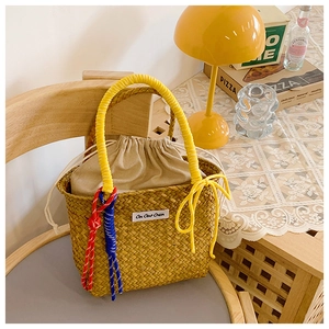 Close-up of handmade straw bucket bag with yellow ring handles and colorful knots