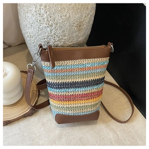 Close-up of a colorful woven straw mini bag with brown leather trim and zipper detail