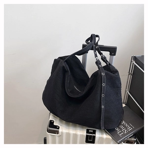 Large black canvas tote bag with metal eyelet strap placed on a white suitcase
