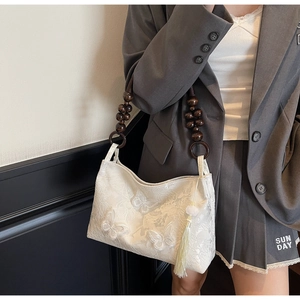 Détail du sac blanc brodé de papillons avec bandoulière en perles de bois sur l'épaule