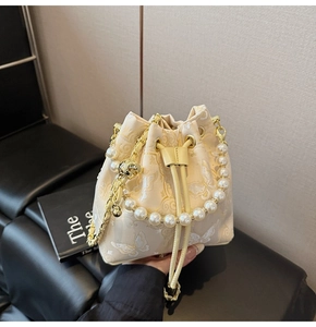 Détail du sac seau crème avec broderie papillon et poignée en perles élégantes