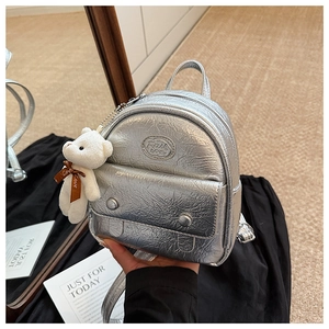 Detailed close-up of metallic silver mini backpack with plush bear and zip pockets