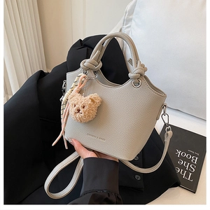 Detail of light gray lychee textured bucket bag with knotted handle and bear charm