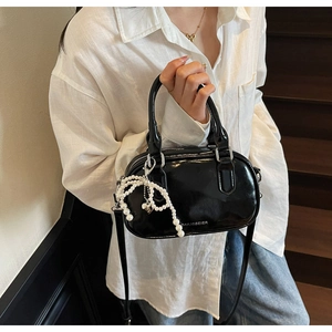 Detail of black glossy leather pillow bag with pearl bow charm and logo branding