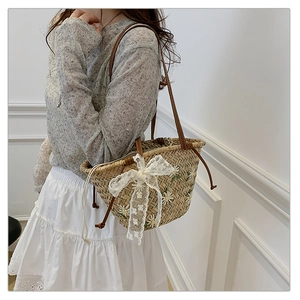 Detail of straw bucket bag with daisy embroidery and a white lace bow on the shoulder