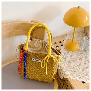 Detail of hand-woven straw bucket bag with logo patch and yellow wrapped handles